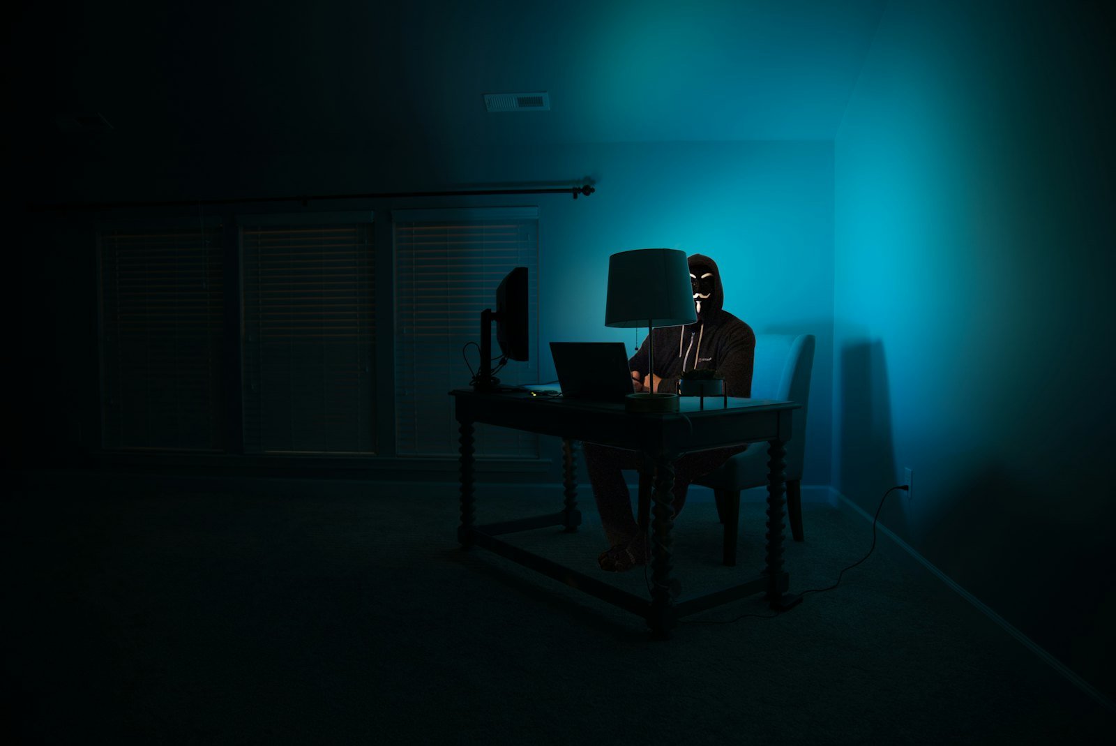 Hooded figure at a laptop in a dark room